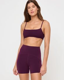 Close-up front view from the knees up of the LSPACE En Pointe Short in plum on a model against a white background, highlighting the waistband and silhouette of the high-waist active shorts.