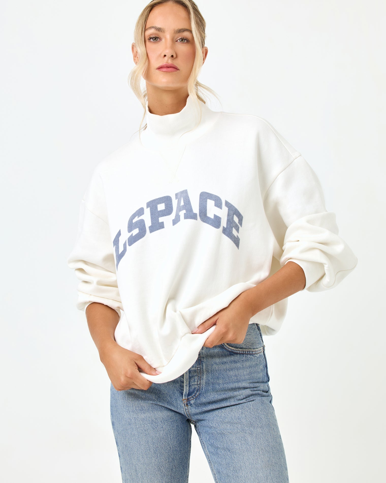 Studio torso view of the Crush Sweatshirt in cream, a cream quarter-zip pullover sweatshirt with "LSPACE" collegiate arch lettering, styled with light blue denim jeans.