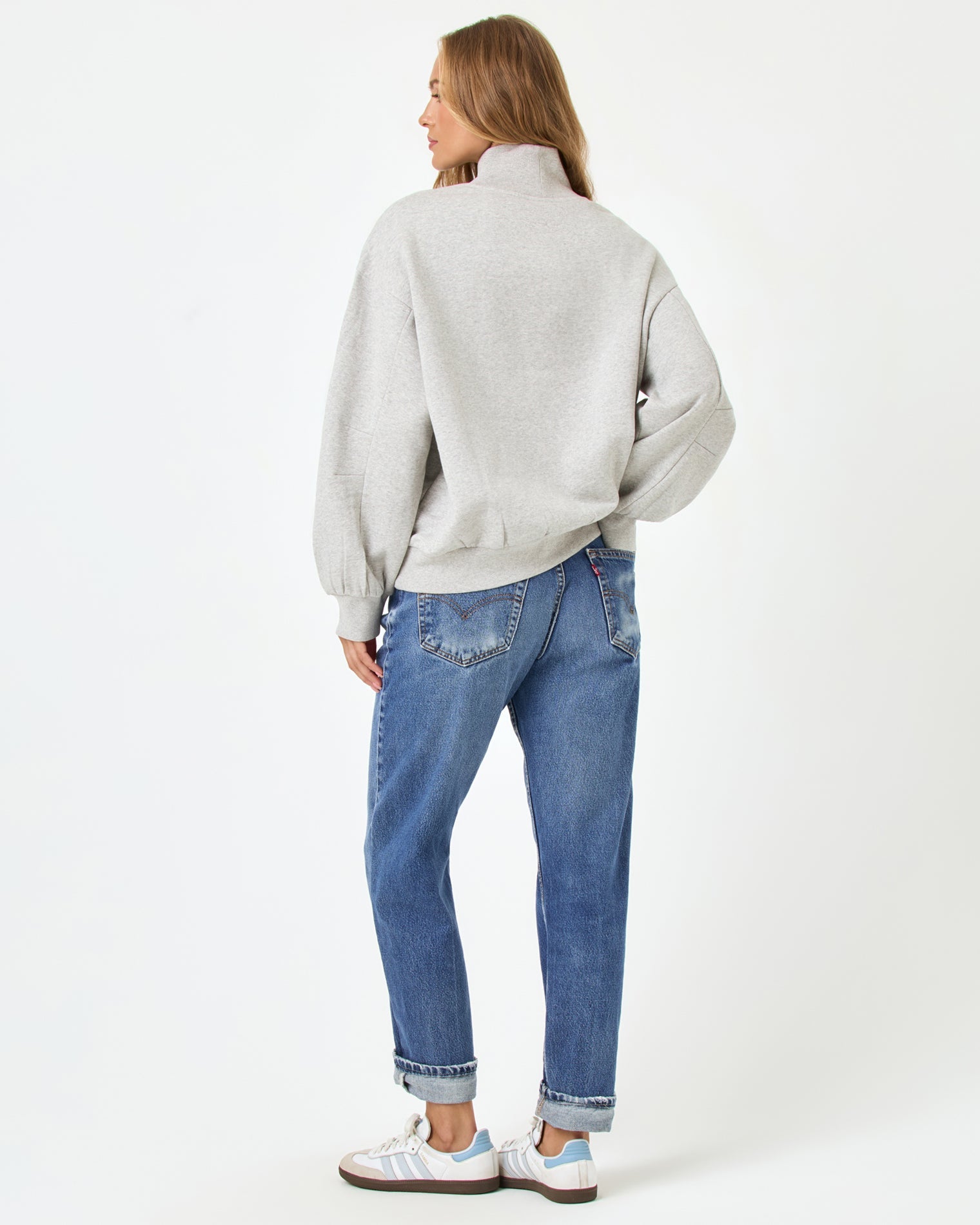 Back full-length studio view of the Crush Sweatshirt in Heather Gray, a heather gray oversized quarter-zip sweatshirt, styled with cuffed blue jeans and Adidas sneakers.