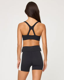 Back view of the LSPACE Uppercut Bra in black-cream on a model against a white background, showing the crossback strap detail, paired with matching black-cream high-rise active shorts.