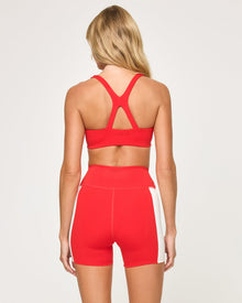 Back view of the LSPACE Uppercut Short in flame-cream on a model against a white background, showing the back of the high-rise active shorts with cream trim, paired with the matching flame-cream sports bra.