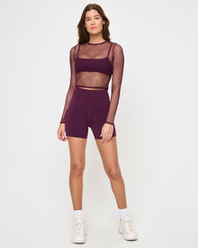 Front view of the LSPACE En Pointe Short in plum on a model against a white background, paired with a plum active pants or leggings, showing an alternate styling option.