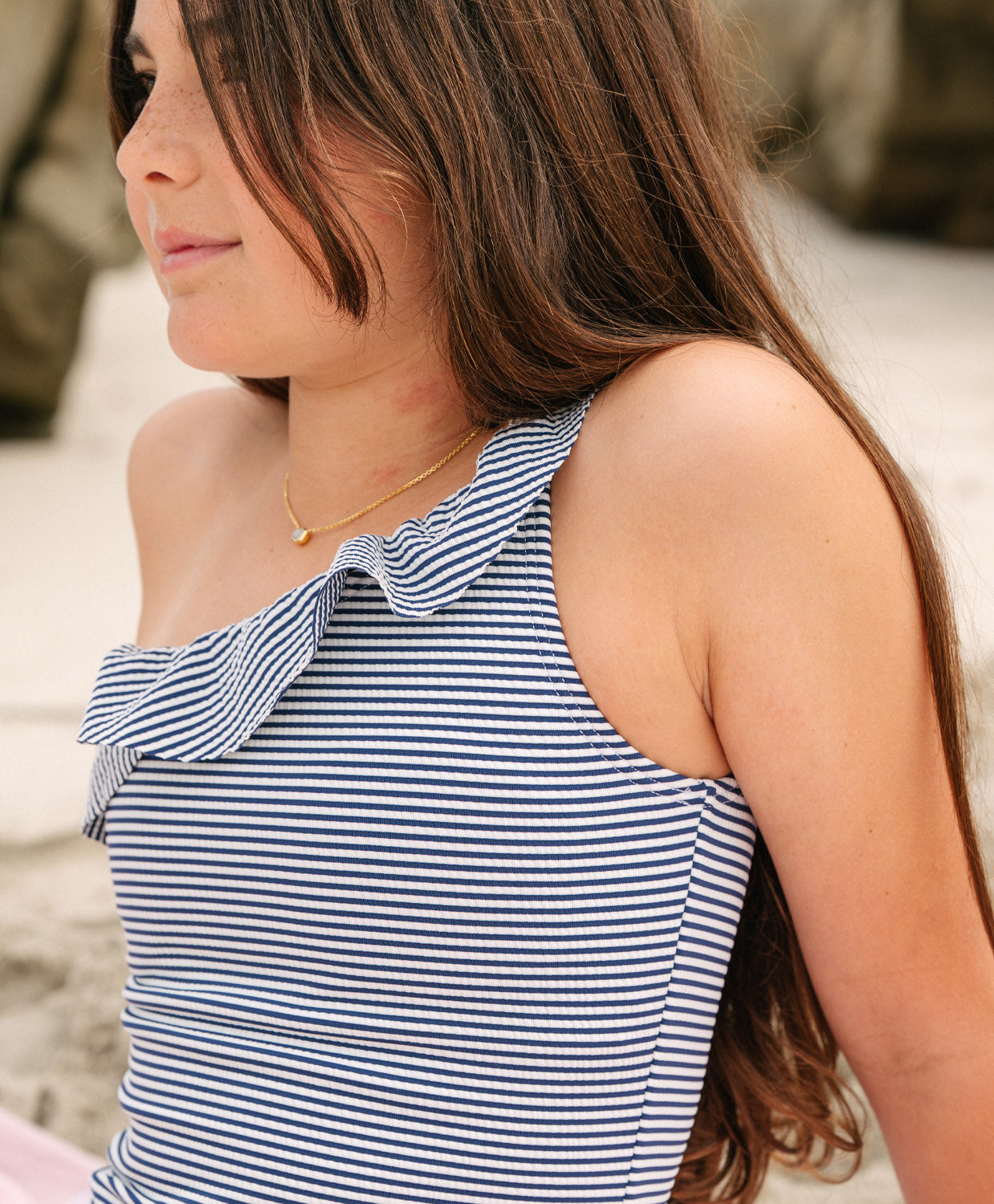 Young girl wearing a striped one piece bikini sitting on the beach.