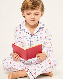 The Kid's Twill Pajama Set in Literary Lessons features a white collared, long-sleeve button-up top and matching pants with a colorful school-themed pattern and navy blue piping accents.