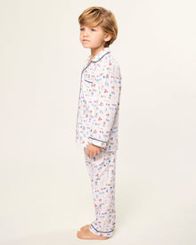 The Kid's Twill Pajama Set in Literary Lessons features a white collared, long-sleeve button-up top and matching pants with a colorful school-themed pattern and navy blue piping accents.