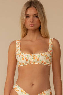 Cream bikini top with orange and green cherry print and ruffled square neckline straps.