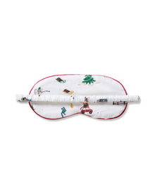 The Kid's Twill Sleep Mask in Holiday Town is a white mask with red trim, decorated with winter scenes of people, a reindeer, a house, a sled, and snowy trees. A small white tag is attached on the right side.