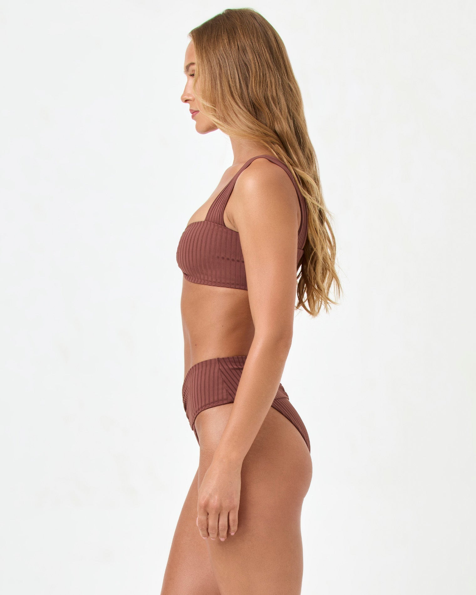 side view of woman wearing a ribbed brown bikini set on a white background