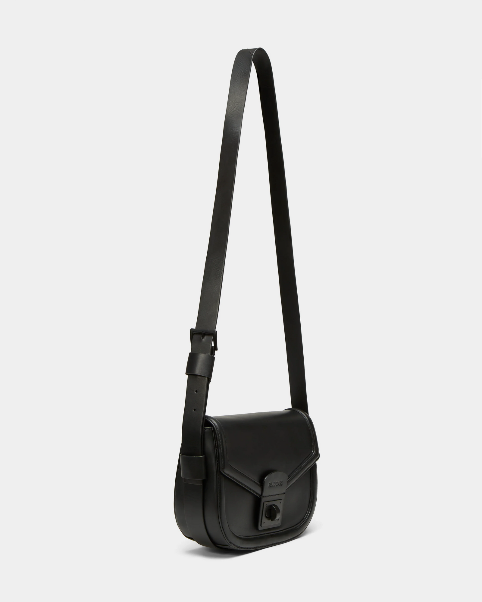 The ALORA - 8324506 Black by Rudsak is a premium leather crossbody bag with an adjustable strap, front flap closure, and rectangular buckle detail. Shown on a plain light background, it exudes timeless elegance.