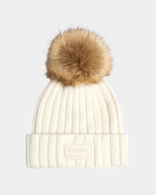 The ANISA - L423500 Optic White by Rudsak is a women's white ribbed knit beanie with a folded brim, brown faux fur pom pom, and a rectangular Rudsak patch on the front. Set against a plain light gray background.