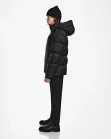 A person in profile faces left, wearing the Rudsak DANIEL M - M124510 Black hooded down puffer jacket with black pants and boots—an ideal winter outerwear choice—set against a plain white background.