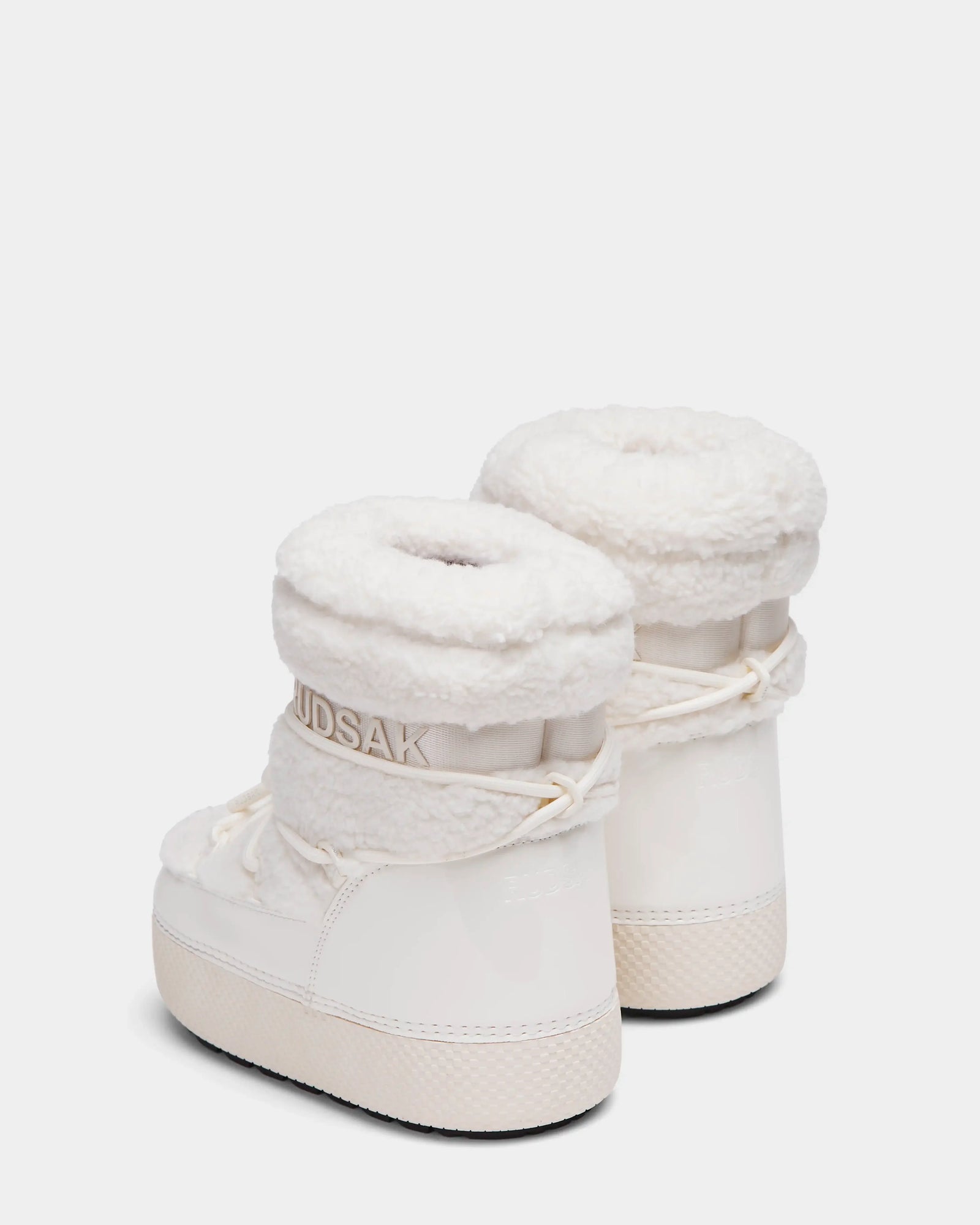 The KATHY Y - 1224500 Iceland boots by Rudsak feature white uppers with thick shearling tops, glossy water-repellent lowers, laces around the ankle, textured soles, and the Rudsak brand near the cuffs.