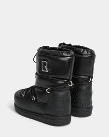 The KIKA - L224506 Black by Rudsak are shiny black winter boots with chunky rubber soles, a large R patch on one boot, Rudsak embossed on the heels, drawstring closures, and stylish rubber detailing.