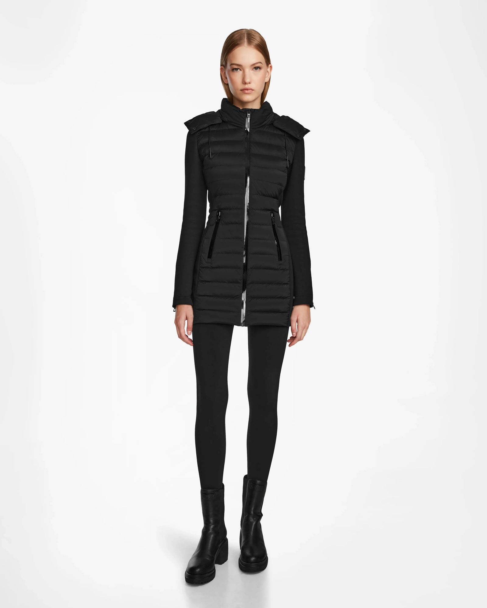 A woman faces forward wearing the RUDSAK MERINA - 8122546 BLACK fitted quilted down jacket with a high collar, paired with black leggings and black ankle boots against a plain white background.