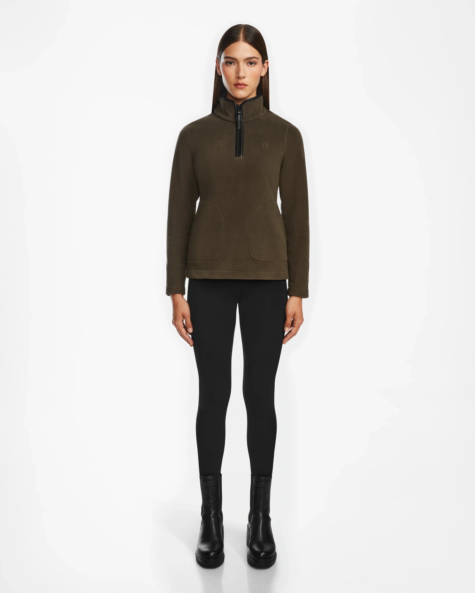 A woman faces forward against a plain white background wearing the Rudsak ORCHID - 8524616 Army dark olive fitted half-zip pullover sweater with vegan leather trims, paired with black leggings and black ankle boots.