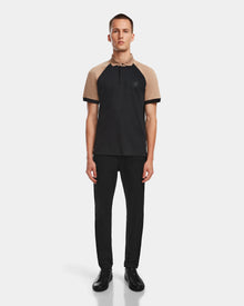 A man faces forward wearing the Rudsak WALTER - 6524531 Black/Camel premium cotton short sleeve polo, paired with black pants and shoes, set against a plain light background.