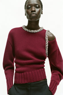 Burgundy knit pullover with crystal beading at neckline and shoulder cutout, paired with black trousers.