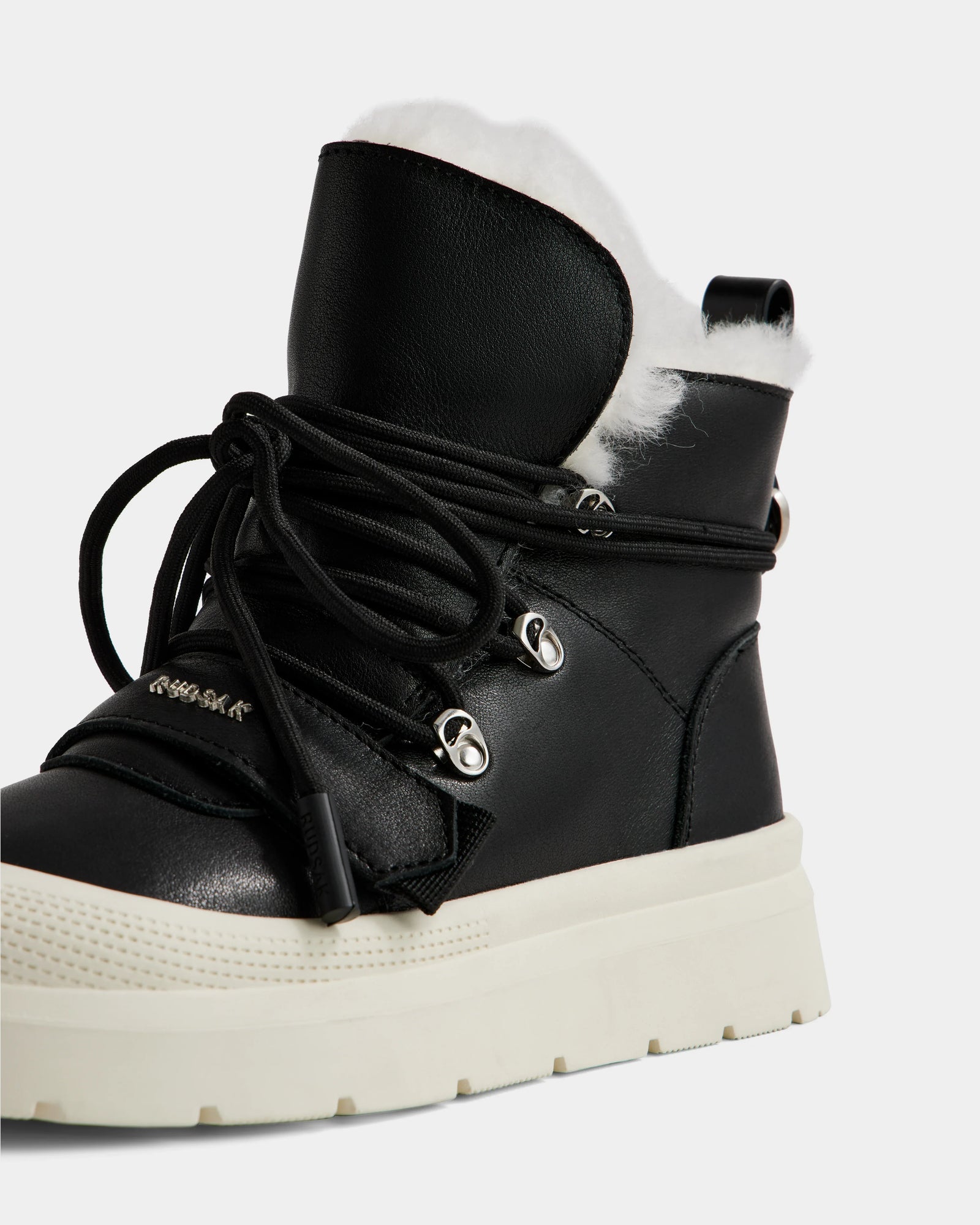 A close-up of the Rudsak ALEXEY L - L225518 Black women’s leather winter boot featuring a thick white sole, silver eyelets, black laces, and plush white faux fur lining visible at the top.