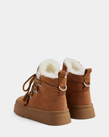 The Rudsak ALEXEY - L225025 Tan women’s suede winter boots feature sturdy rubber soles, plush wool lining, metal lace hooks, and pull tabs, shown against a plain light background.