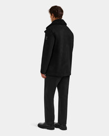 A man stands with his back to the camera, wearing the Rudsak ELTON - M125534 Black faux shearling coat, along with black pants and shoes, set against a plain light gray background.