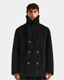 A person wearing the Rudsak ELTON - M125534 Black double-breasted overcoat with a high collar stands against a plain light background, looking straight at the camera.