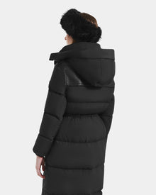 A woman is shown from the back wearing the Rudsak EMBER M-L - L125543 Black long down puffer coat with removable hood and a black furry hat, set against a plain light background.