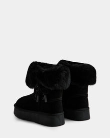 The Rudsak INESA - L225026 Black women's suede platform boots feature thick faux fur cuffs, flat soles, cozy wool lining, and decorative side bows. Shown on a white background.