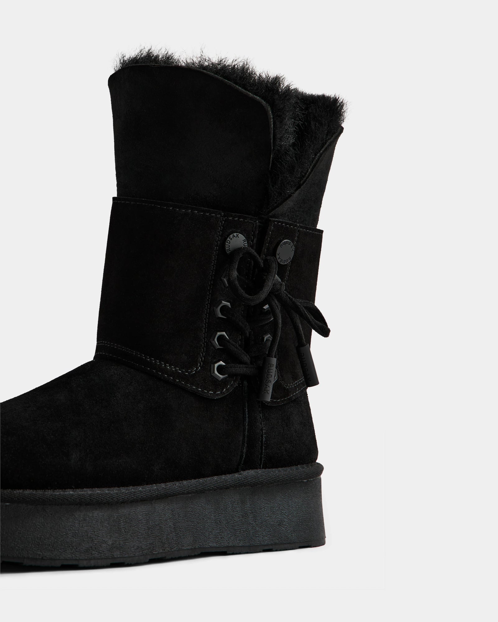The Rudsak INESA - L225026 Black is a women's suede platform boot with a wool lining, thick sole, and ankle lace-up detail, shown on a plain white background.