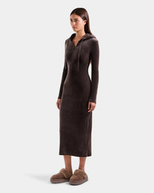 A woman wears the Rudsak ISABELLA - L525502 velour hooded midi dress in Espresso, paired with light brown fuzzy slippers. She stands facing slightly right against a plain light background.