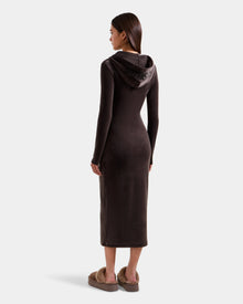 A woman faces away in the Rudsak ISABELLA - L525502 Espresso women's velour hooded midi dress, paired with brown fuzzy slippers. Her straight hair is down as she poses against a plain light gray background.