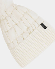 A close-up of the Rudsak LANYA - L423514 Iceland white quilted winter hat, featuring a ribbed knit fold-over cuff with a small black tag; its wool blend knit and quilted textures are clearly visible.
