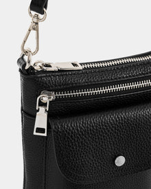 Close-up of the Rudsak LILA - L325513 Black women’s crossbody bag in black pebbled leather with a front flap pocket, silver zipper, metal clasp fastenings, adjustable strap, and visible hardware details.
