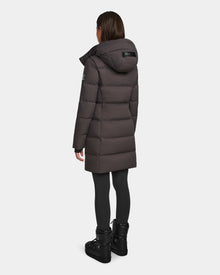 A person wearing the Rudsak MIRIAM - L123544 Grey womens down puffer coat with a hood, paired with black leggings and black boots, stands facing away from the camera against a plain white background.