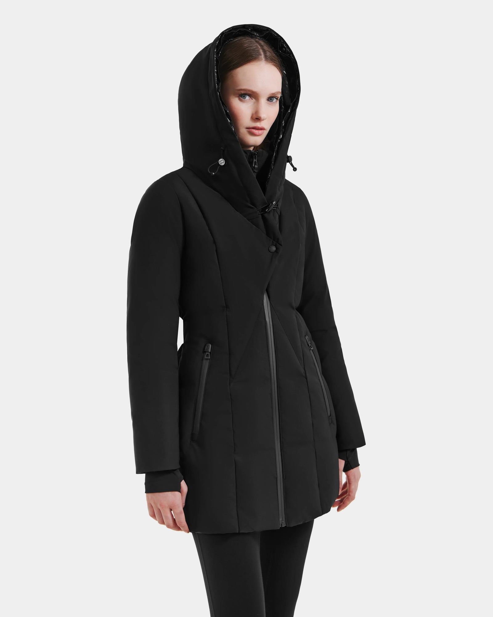 A person wearing the Rudsak MODA M - L125555 Black, a long, black, hooded down puffer winter coat with a front zipper and side pockets, stands against a plain light background.