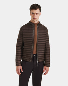 A man wearing the Rudsak REYMOND M - M125523 Mocha dark brown, RDS-certified down puffer jacket over a tan sweater and black pants stands against a plain white background.