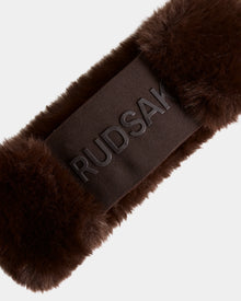 Close-up of the SANDIE - L425552 Espresso headband by Rudsak, featuring brown faux fur and a smooth dark band with raised RUDSAK text at the center. The stylish women’s winter accessory is set against a plain, light background.