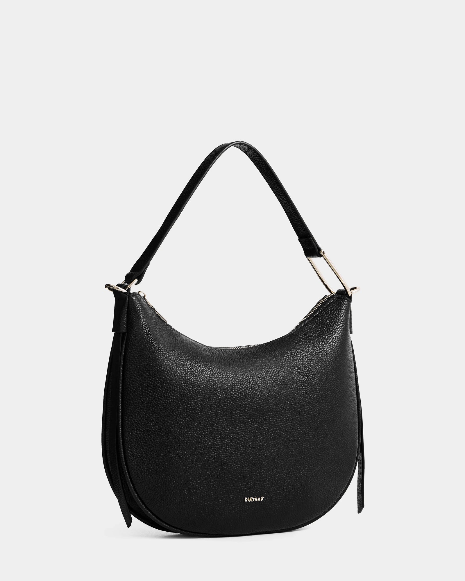 The Rudsak SYLVIA - L325515 Black is a black crescent leather handbag featuring a single short strap, gold-tone hardware, and subtle branding, displayed on a plain light gray background.