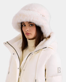 A woman wears the Rudsak YURI - L425538 Iceland white puffer jacket with vegan-leather trim and a faux-fur bucket hat, posing against a light background—a chic winter look.