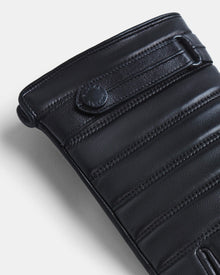 Close-up of the CORTES - 6418506 BLACK by Rudsak: black leather with horizontal padding, precise stitching, a snap button embossed with the Rudsak logo, smooth texture, and rounded edges—reflecting premium craftsmanship in Rudsak gloves.