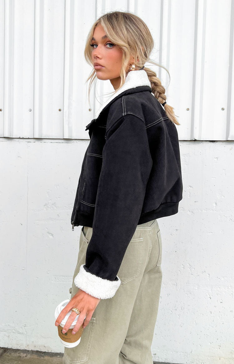 Side view of a black denim jacket with white sherpa collar and cuffs, showing white contrast stitching