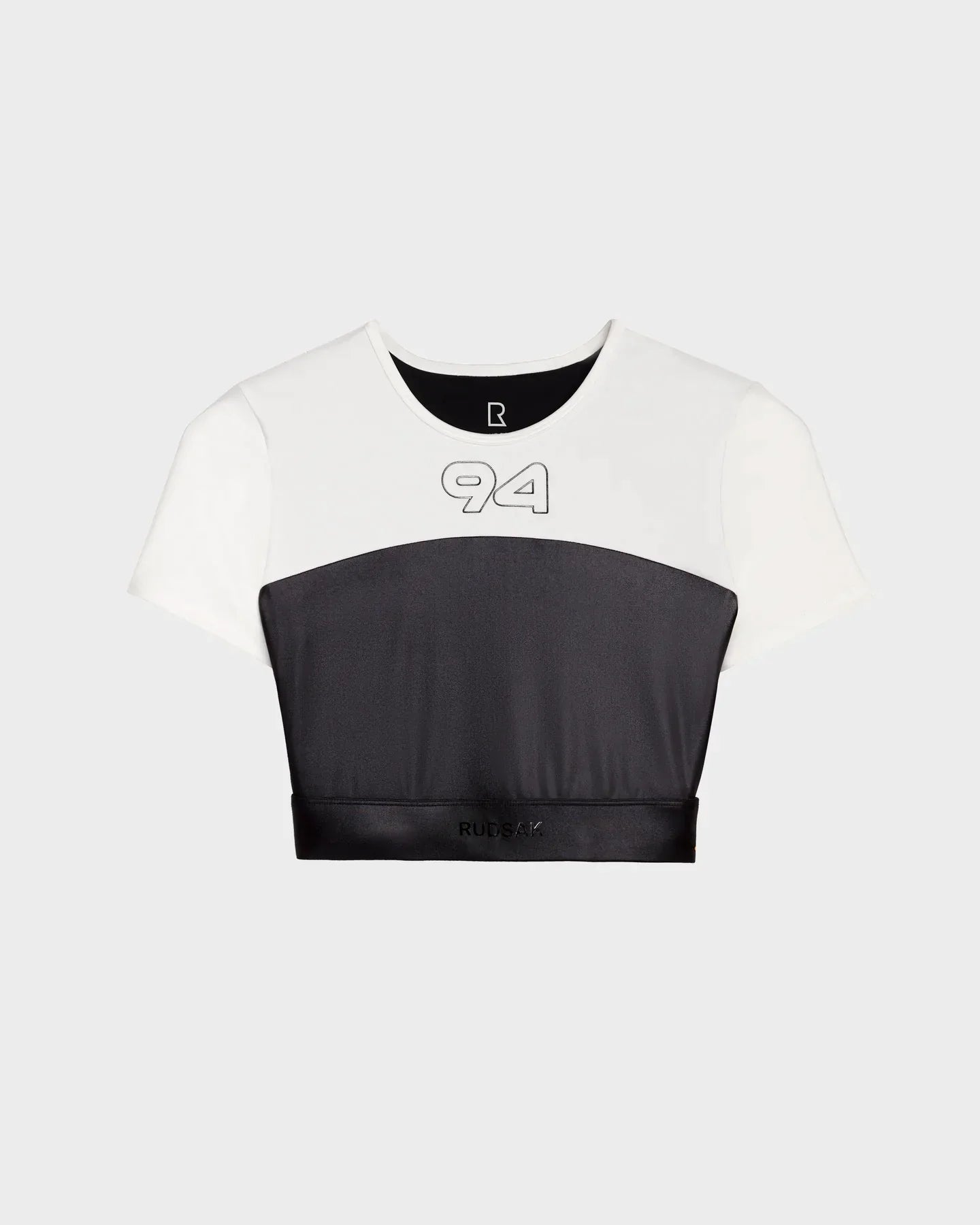 The LILIANE - 8524018 Black by Rudsak is a women’s short-sleeve fitted crop top with a white upper half, black lower half, light gray “94” on the chest, and subtle RUBÉA branding on the bottom black band.