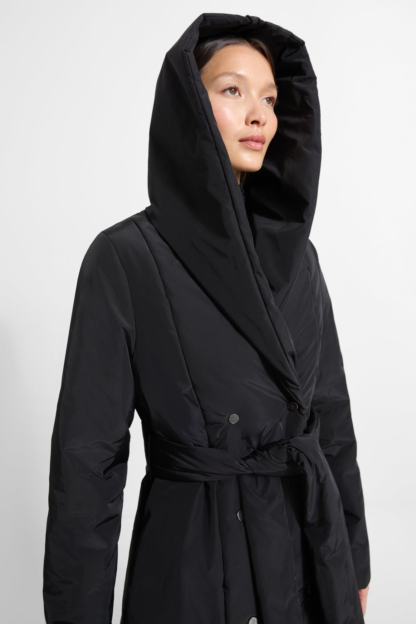 Black hooded puffer jacket with drawstring waist and button closure, worn with hood up.