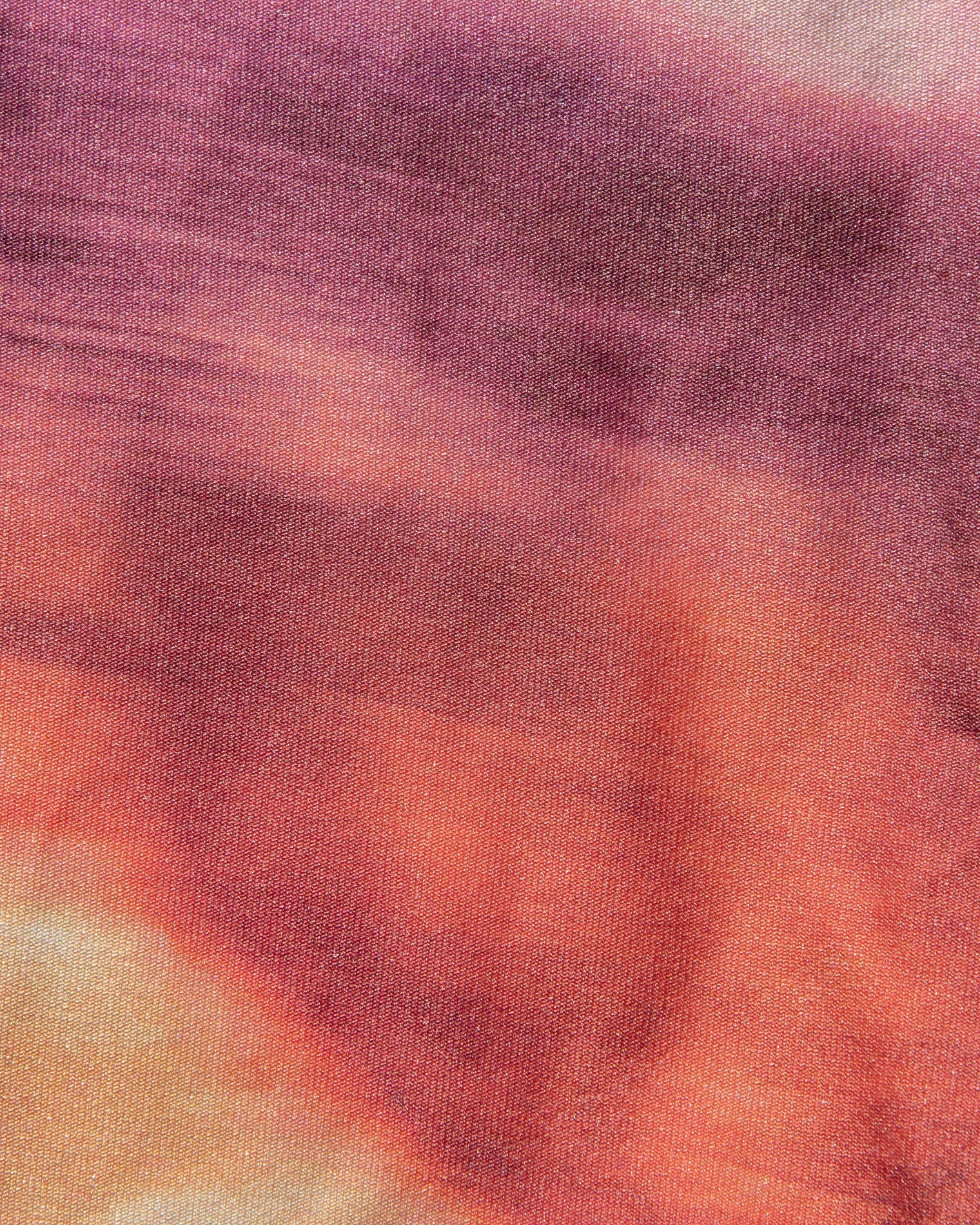 Close-up of a fabric with a tie-dye pattern in shades of purple, orange, and pink.