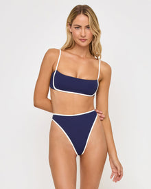 front view of woman wearing a white and navy bikini against a plain background