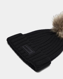 The ANISA - L423500 Black/Natural by Rudsak is a black ribbed knit beanie with a folded brim, rectangular Rudsak patch, and large faux fur pom pom—an elevated, stylish pick for women’s winter accessories.