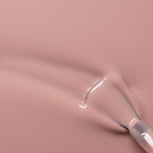 A close-up of a nail polish brush spreading glossy, nude-pink nail polish on a smooth surface.