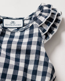 Close-up of a navy gingham print dress with ruffled sleeves. This lightweight twill nightgown has a fabric label at the neckline with Petite Plume and a small bird illustration, featuring a soft, textured appearance.