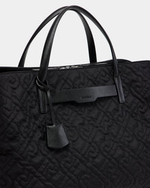 Close-up of the Rudsak ASMINE - L325005 Black tote with an embossed monogram pattern, two leather handles, a leather tag, and a branded leather accent near the top.