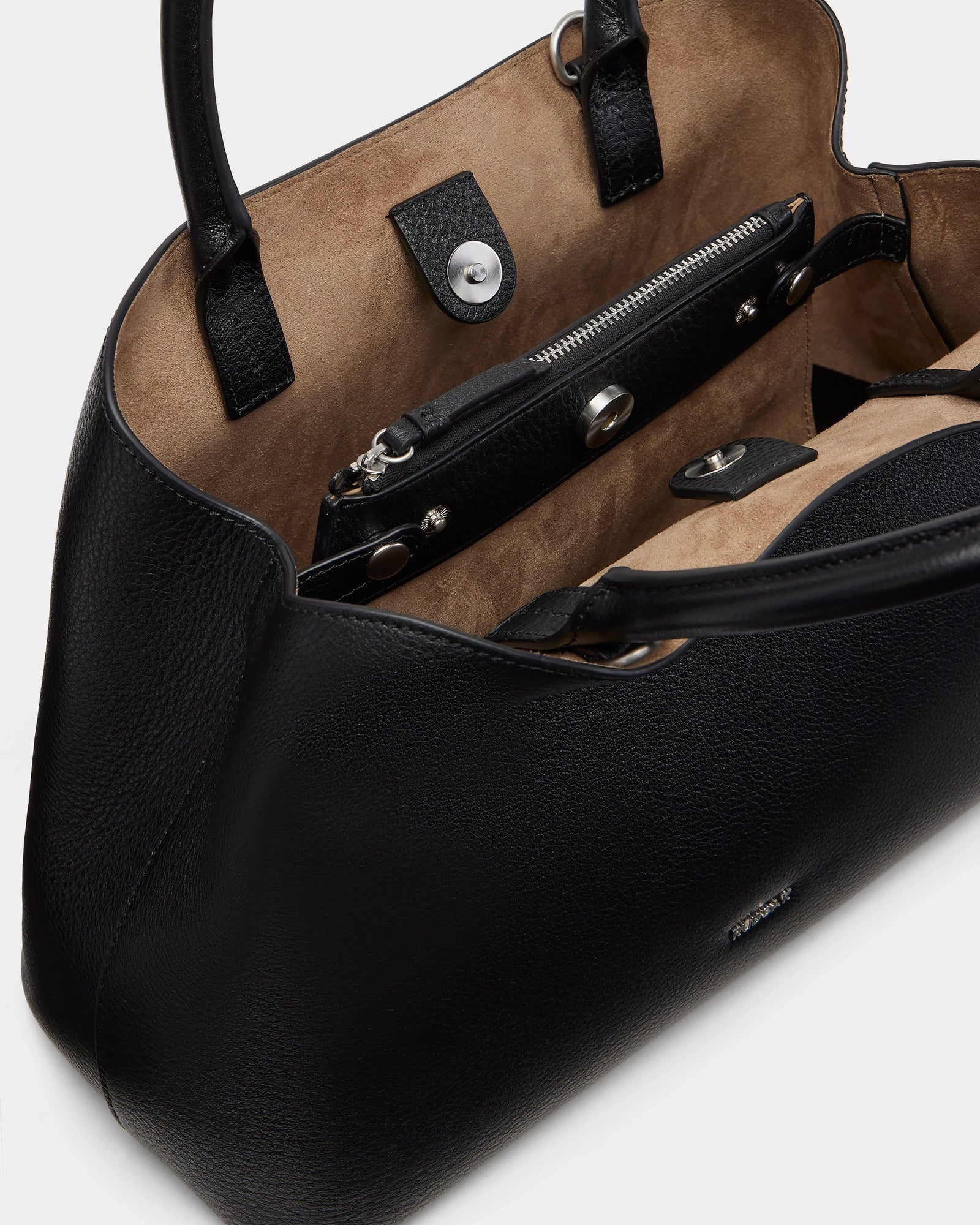 A close-up of the Rudsak CATIRA S - 8325006 Black women’s tote bag in black pebble leather with tan suede lining, featuring a zippered inner pocket, snap closures, sturdy handles, and a removable shoulder strap for versatility.