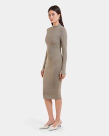 A woman stands slightly to the side, wearing the MAYLIN - 8523504 Cement Pattern dress by Rudsak, paired with white pointed-toe heels and drop earrings, against a plain white background.